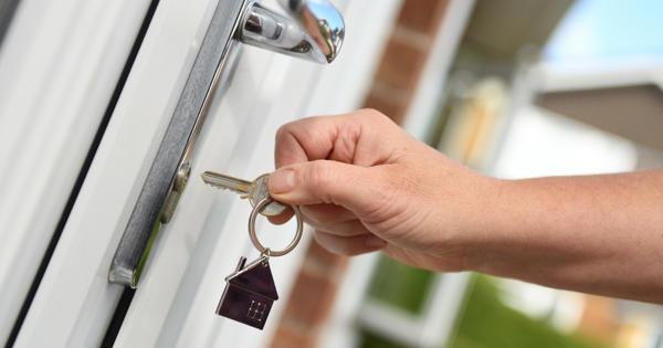 A picture of a persons hand that is just about to put a key in a door to unlock it on a sunny day