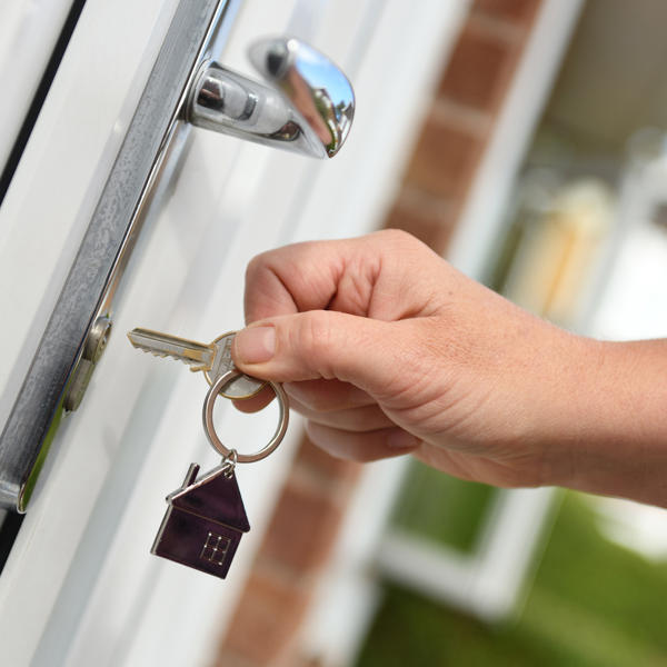 A picture of a persons hand that is just about to put a key in a door to unlock it on a sunny day