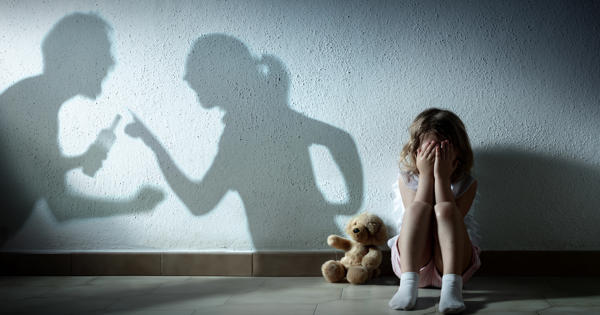 A picture of a little girl that is scared holding her head in her hands. There is a shadow of man holding what appears to be a bottle of alcahol clenching his fist arguing with a woman