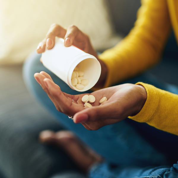 A close up picture of a person sat cross legged emptying pills into their hand