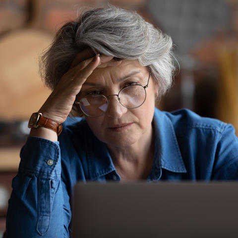 Older lady looking worried on laptop - stock